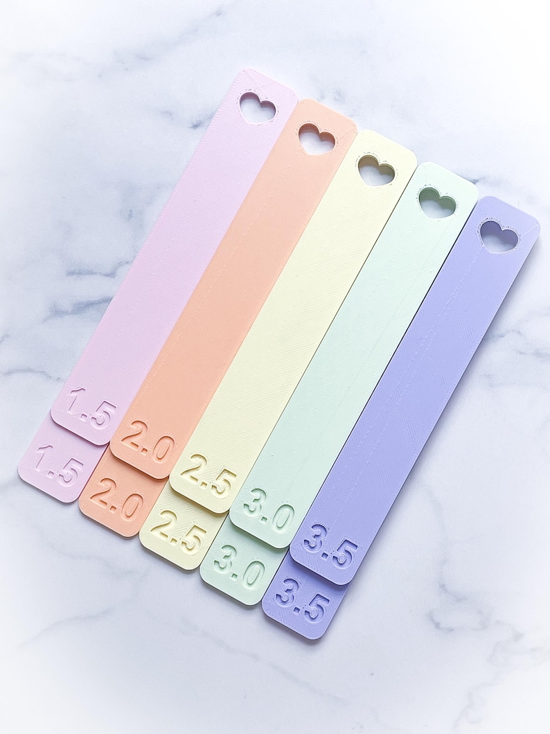 May include: Five pastel-colored measuring sticks with heart cutouts. The sticks are labeled with numbers from 1.5 to 3.5.