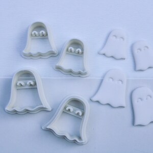 May include: A selection of white ghost-shaped cookie cutters and fondant decorations. The cutters have a scalloped bottom edge and eye details. The fondant ghosts have a simple, rounded shape with eye details. Ideal for Halloween baking and cake decorating.
