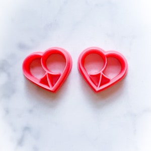 Op de afbeelding: Twee roze hartvormige koekjesvormen met een kleinere hartvormige uitsnijding in elk.