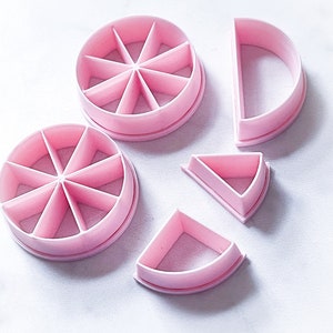 May include: A collection of pink plastic cake and pie cutters. The set includes two circular cutters divided into segments, a half-circle, and two pie-shaped cutters. These tools are designed for baking and crafting.