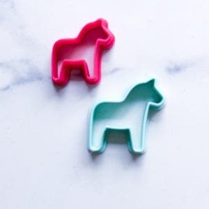 Puede incluir: Dos cortadores de galletas con forma de caballo, uno rosa brillante y otro turquesa. Los cortadores son de plástico y presentan un contorno sencillo de un caballo. Ideales para hornear o manualidades. Colores vibrantes y atractivos.
