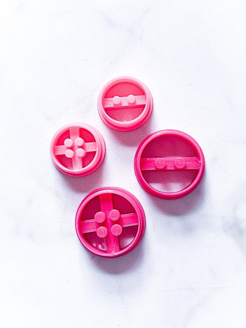 May include: Four pink plastic cookie cutters shaped like Lego bricks. The cutters are different sizes and have different numbers of studs.
