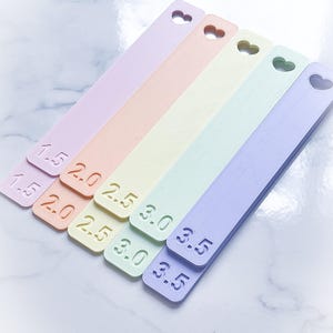 May include: Six pastel-colored plastic rulers with heart-shaped cutouts at the top. The rulers are labeled with measurements in inches: 1.5, 2.0, 2.5, 3.0, 3.5, and 3.5.