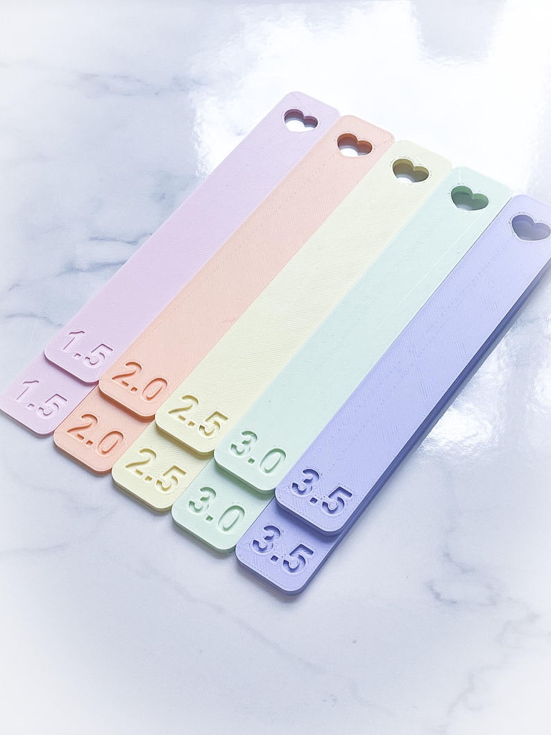 May include: Six pastel-colored plastic rulers with heart-shaped cutouts at the top. The rulers are labeled with measurements in inches: 1.5, 2.0, 2.5, 3.0, 3.5, and 3.5.