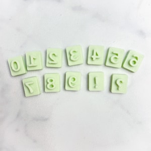 May include: A set of ten light green plastic number stamps, arranged in a semi-circle. The numbers are 0 through 9.