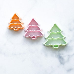 May include: Three Christmas tree cookie cutters, one orange, one pink, and one green.