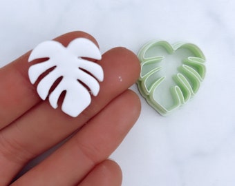 Könnte beinhalten: Ein weißer Monstera-Blatt-Ausstecher aus Kunststoff und ein grüner Monstera-Blatt-Ausstecher aus Kunststoff.