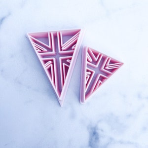 Puede incluir: Dos cortadores de galletas triangulares de plástico rosa con un diseño geométrico.
