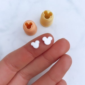 May include: Two white plastic Mickey Mouse head shapes, and two plastic molds for making the shapes, one yellow and one orange.