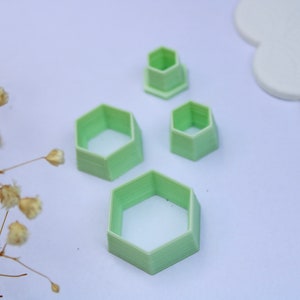 May include: Four green plastic hexagon-shaped cookie cutters of different sizes. The cutters are on a white surface.