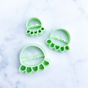 May include: Three green plastic cookie cutters shaped like smiling octopuses of different sizes.