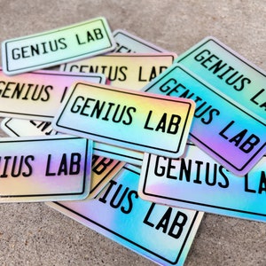 May include: A pile of iridescent holographic stickers with the text "Genius Lab" printed in black.