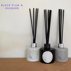 May include: Three diffuser bottles with black reeds. The bottles are white, black, and grey with a silver cap. Each bottle has a white circle label with the text "NEW DAWN" and a leaf design.