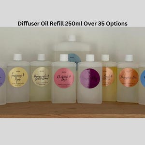 May include: Ten clear glass bottles with labels containing different scents for a diffuser. The bottles are arranged in a row on a wooden surface. The labels have different colours and designs. The text on the labels reads: Lavender,  Frankincense & Myrrh, Honeycrisp & Green Almond,  Rhubarb & Rose,  Black Currant &  Grapefruit,  Peach & Nectarine,  Pumpkin Pie,  Big  Caramel &  Brown Sugar.