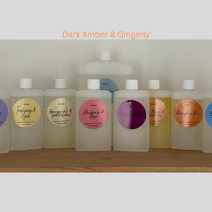 May include: Ten clear glass bottles with white labels and black text. The labels have different scents, including Lavender, Raspberry & Rose, and Big Curl & Gingerly. The bottles are arranged in a row on a wooden surface.