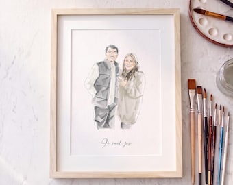 May include: A framed watercolor portrait of a couple standing side by side, with the man wearing a vest and the woman in a sweater. The text "She said yes" is written in cursive script at the bottom of the illustration within the light wood frame.
