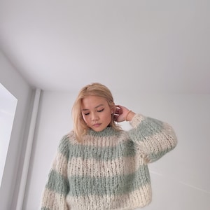 May include: A light green and white striped sweater with a fluffy texture. The sweater has a high neck and long sleeves.