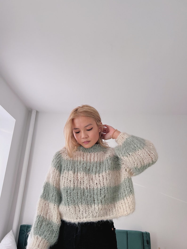 May include: A light green and white striped sweater with a fluffy texture. The sweater has a high neck and long sleeves.