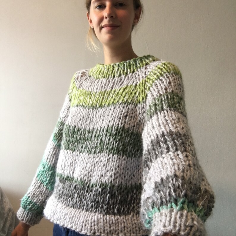 May include: A striped sweater with green, gray, and white stripes. The sweater has a round neckline and long sleeves.