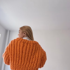 K&ouml;nnte beinhalten: Ein knallorangefarbener, grob gestrickter Cardigan in Cropped-L&auml;nge. Der Cardigan ist aus dickem Garn gefertigt und hat eine lockere Passform.