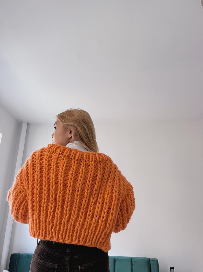 K&ouml;nnte beinhalten: Ein knallorangefarbener, grob gestrickter Cardigan in Cropped-L&auml;nge. Der Cardigan ist aus dickem Garn gefertigt und hat eine lockere Passform.