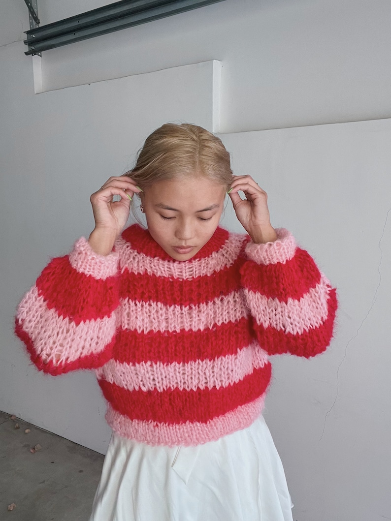 May include: A pink and red striped fuzzy sweater with a loose fit and long sleeves.