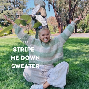 Könnte beinhalten: Eine Frau trägt einen grün-weiß gestreiften Pullover mit dem Text "STRIPE ME DOWN SWEATER" auf der Vorderseite. Sie sitzt auf dem Gras mit ausgestreckten Armen.