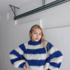 May include: A blue and white striped knit sweater with a high neck and long sleeves. The sweater is made of a soft, fluffy yarn.