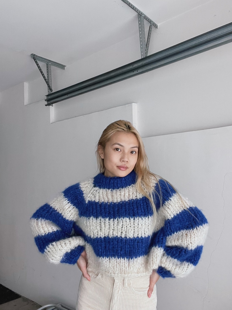 May include: A blue and white striped knit sweater with a high neck and long sleeves. The sweater is made of a soft, fluffy yarn.