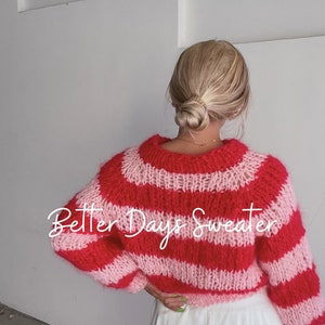 May include: A pink and red striped knit sweater with the text "Better Days Sweater" on the back. The sweater is cropped and has a loose fit.