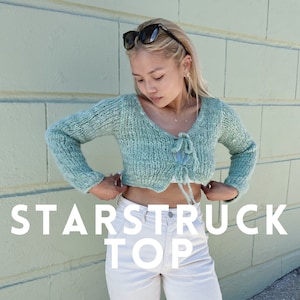 May include: A light blue knitted crop top with a tie detail at the front. The top is worn with white trousers and the text "STARSTRUCK TOP" is superimposed on the image. The text "KARAS.KNIT.ENG" is also visible at the bottom of the image.