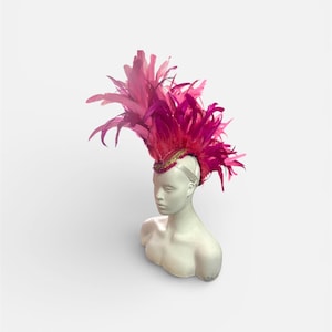 Peut inclure: Coiffe de plumes rose vif avec une bande dorée et ornée de bijoux, présentée sur une tête de mannequin blanche. Les plumes fuchsia créent un accessoire saisissant. Ce chapeau est conçu pour les événements spéciaux.