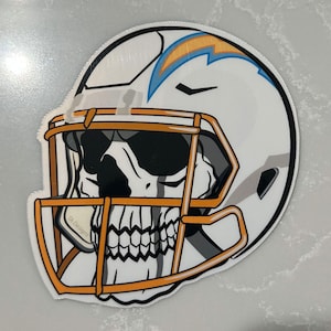 May include: A white football helmet with a blue and yellow lightning bolt design. A skull is visible inside the helmet with a black and white design. The helmet has a gold face mask.
