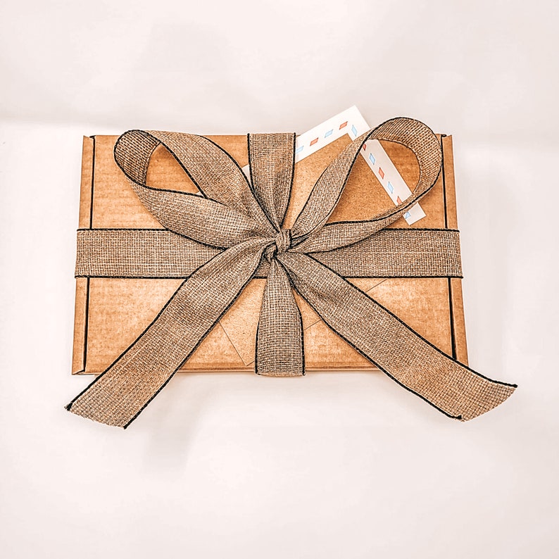 May include: A brown cardboard box with a brown and black ribbon tied in a bow. The box is wrapped in a brown paper with a black border.