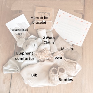 May include: A gift box for a new parent with a gray elephant comforter, a white bib, a beige vest, a muslin cloth, two washcloths, booties, and a card that says "Congratulations Mummy to be bracelet".