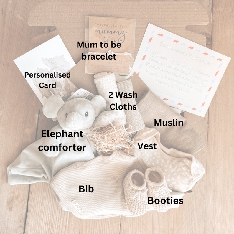 May include: A gift box for a new parent with a gray elephant comforter, a white bib, a beige vest, a muslin cloth, two washcloths, booties, and a card that says "Congratulations Mummy to be bracelet".
