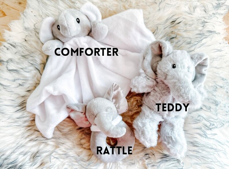 Puede incluir: Un conjunto de tres juguetes de peluche de elefante. El primero es una manta blanca con una cabeza de elefante gris unida. El segundo es un oso de peluche de elefante gris. El tercero es un sonajero de elefante gris.