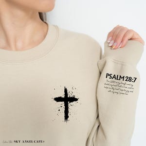 May include: Beige sweatshirt with a black cross graphic and the text "PSALM 28:7 The LORD is my strength and my shield, my heart trusts in him, and he helps me. My heart leaps for joy, and with my song I praise him."