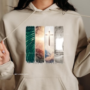 Può includere: Una felpa con cappuccio beige con una stampa grafica di una croce, foglie di palma e una tomba di pietra. Il testo "He Did It All For Me" è stampato sotto la grafica.