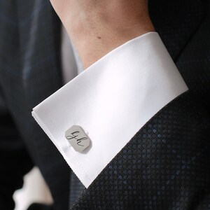 May include: A white dress shirt with a pair of silver cufflinks featuring the initials "LJH" in cursive.