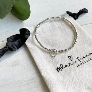 May include: A silver beaded bracelet with a small heart charm. The bracelet is in a white drawstring bag with the text "Mari Fiona Jewellery" printed on it.