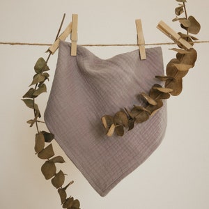 May include: A soft, light purple muslin cloth hanging on a clothesline with wooden clothespins. Dried eucalyptus leaves are draped over the cloth and the clothesline.