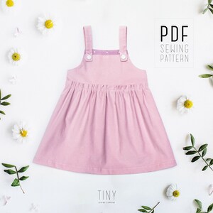 May include: A pink sleeveless dress with a gathered skirt and two buttons on the straps. The dress is made from a soft, lightweight fabric and has a simple, classic design. The text "PDF SEWING PATTERN" is visible in the upper right corner of the image.