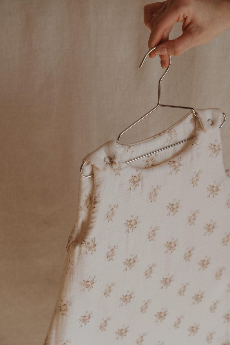 May include: A white sleeveless sleep sack with a delicate brown floral pattern hanging on a silver hanger.