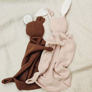 K&ouml;nnte beinhalten: Zwei weiche Pl&uuml;schtiere in Form eines B&auml;ren und eines Hasen. Der B&auml;r ist braun und der Hase ist rosa. Beide Spielzeuge haben wei&szlig;e Ohren und sind aus einem weichen, strukturierten Stoff gefertigt.