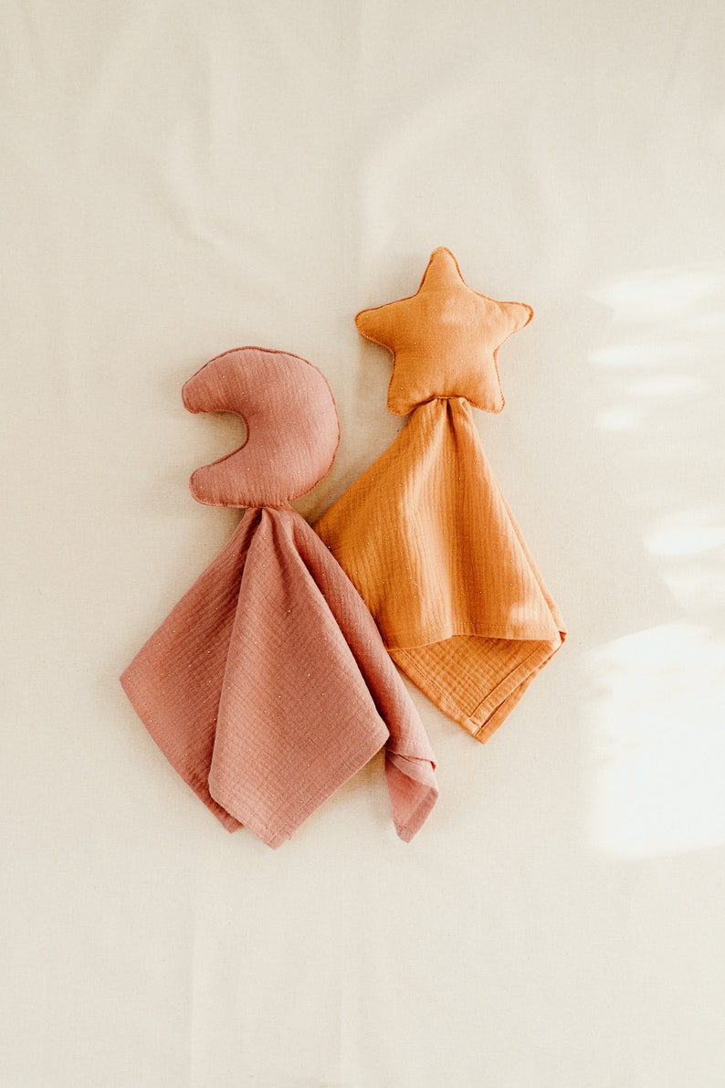 May include: Two baby blankets with a star and crescent moon design. The star blanket is orange and the moon blanket is pink.