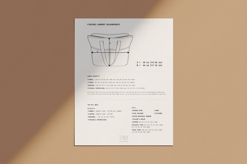 May include: A black and white line drawing of a tote bag with measurements in inches and centimeters. The drawing shows the finished garment measurements for the bag, including the height and width. The text "FINISHED GARMENT MEASUREMENTS" is at the top of the page. The text "TINY" is at the bottom of the page.