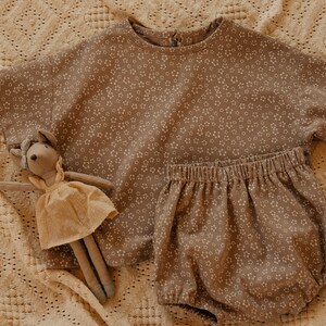 May include: A brown and white floral print baby outfit with a short-sleeved top and bloomers. A plush toy mouse is lying on the fabric.