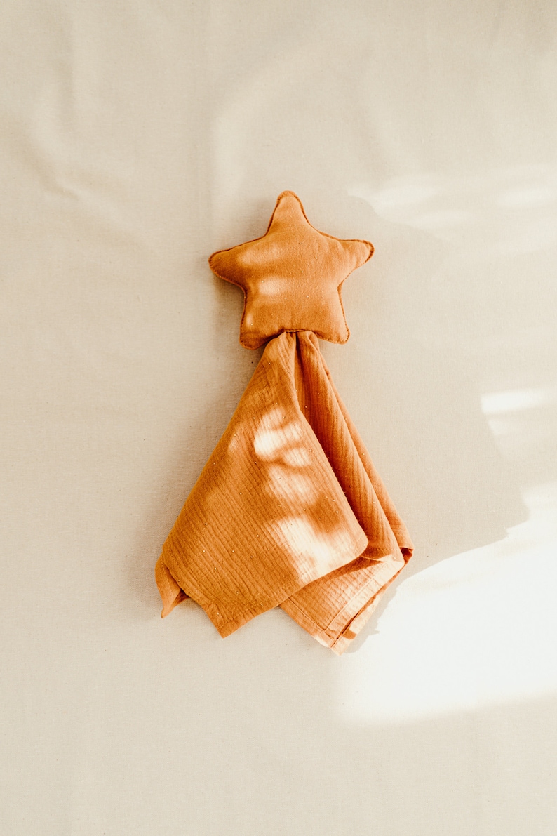 May include: A soft, orange star-shaped baby blanket with a textured surface. The blanket is folded and the star is at the top.