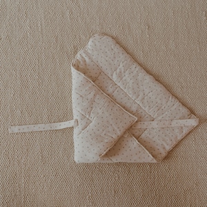 May include: A beige quilted baby blanket with a small floral pattern. The blanket is folded in half and tied with a ribbon.